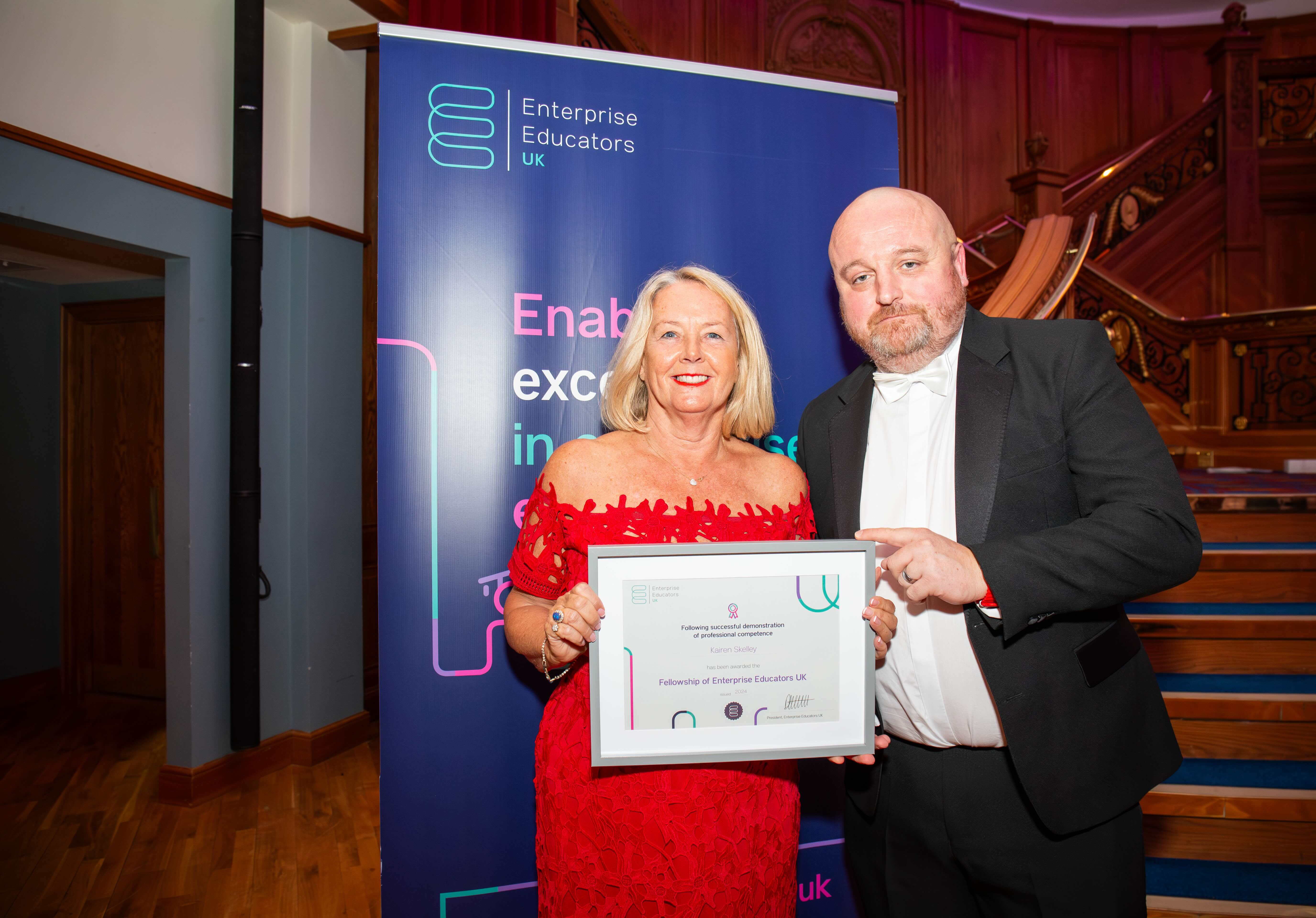 Kairen Sculley is awarded her EEUK Fellowship by President Dave Bolton. Kairen is wearing a stunning red dress and Dave is dressed smartly. Kairen is holding her EEUK Fellowship certificate.