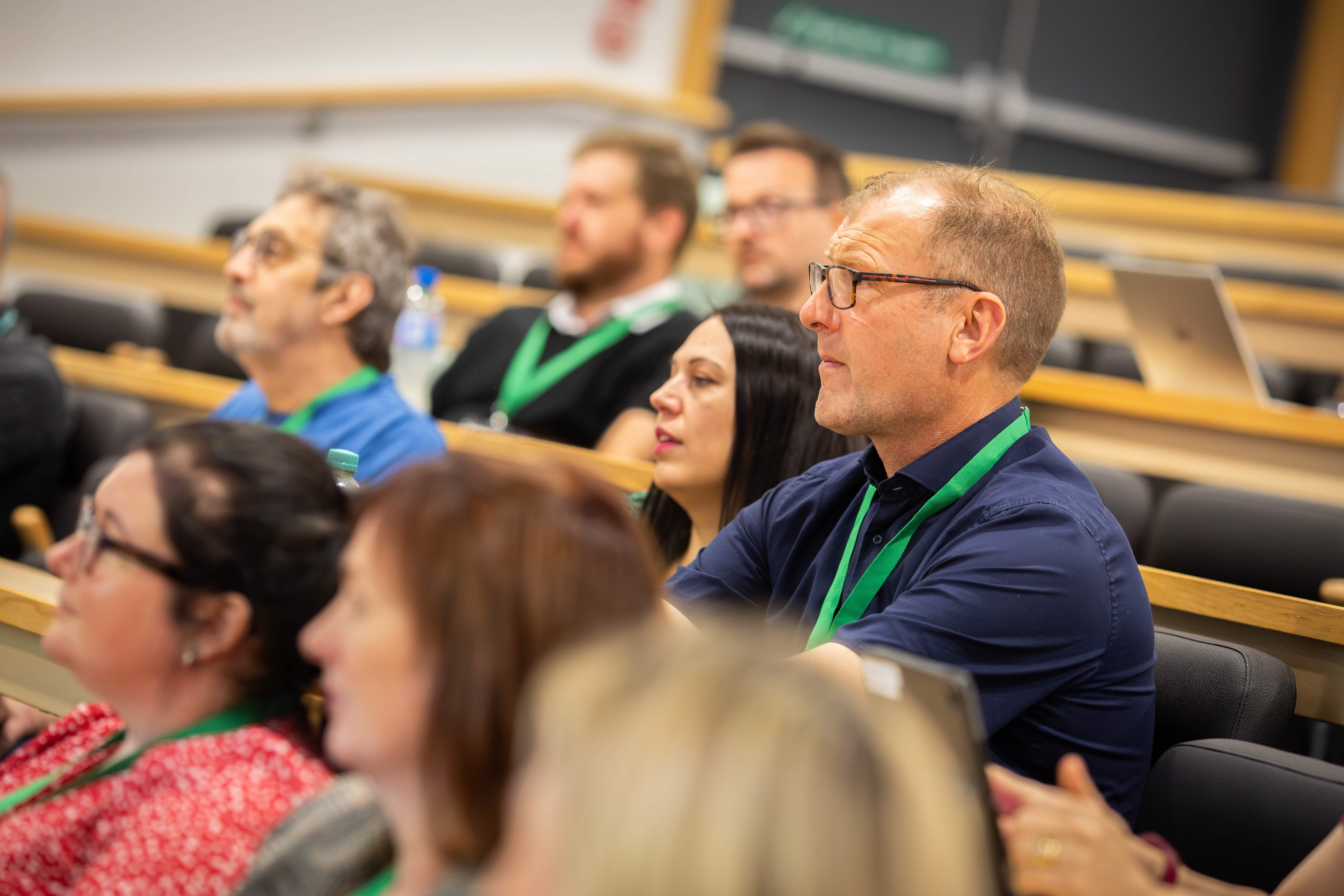 Delegates in a themed parallel session. They are seated in a tiered lecture theatre and looking at a presenter's talk.